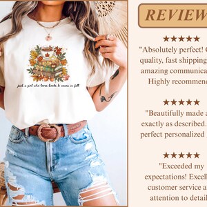 May include: A cream-colored t-shirt featuring a graphic of a stack of books topped with a mug of cocoa surrounded by autumn leaves. The text below the graphic reads, "just a girl who loves books & cocoa in fall." The shirt is paired with blue jeans.