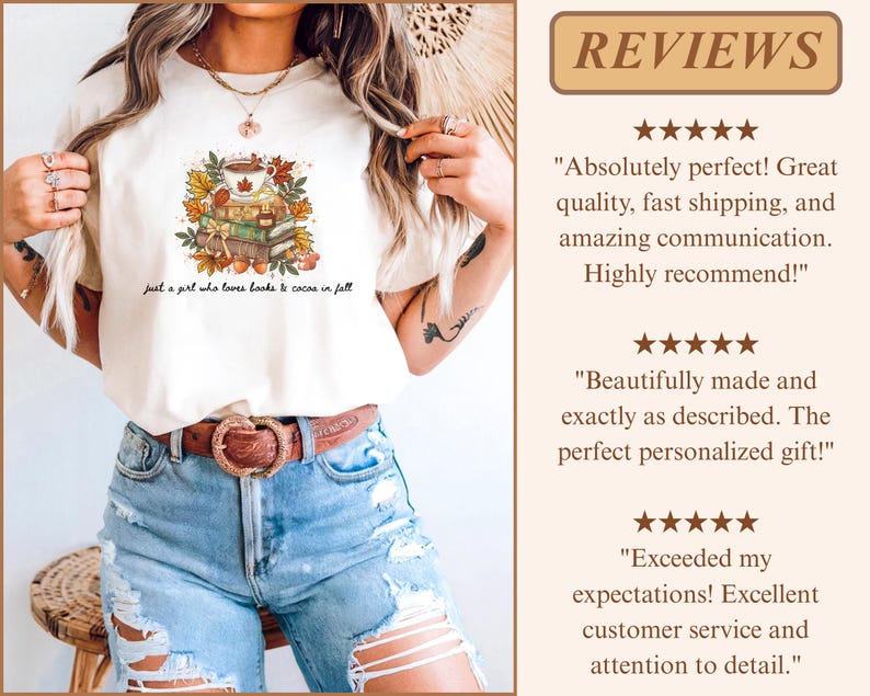 May include: A cream-colored t-shirt featuring a graphic of a stack of books topped with a mug of cocoa surrounded by autumn leaves. The text below the graphic reads, "just a girl who loves books & cocoa in fall." The shirt is paired with blue jeans.