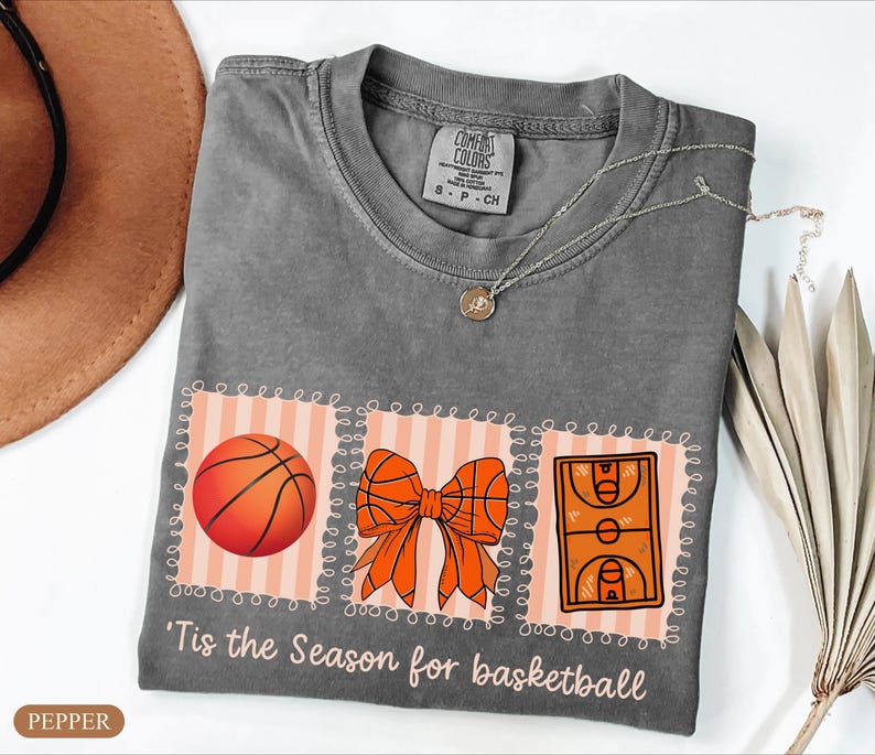 Peut inclure: Un t-shirt gris Comfort Colors avec un motif sur le th&egrave;me du basketball. Le motif comprend un ballon de basket, un n&oelig;ud et une illustration d'un terrain de basket. Le texte "'Tis the Season for basketball" est imprim&eacute; en dessous.