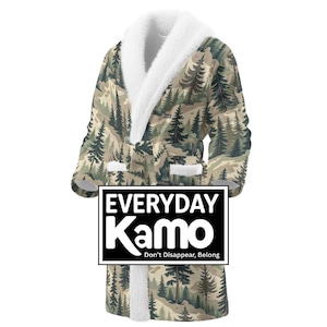 May include: A plush, hooded robe with a camouflage pattern featuring a forest scene in shades of green, brown, and beige. The robe has a white, fluffy collar and cuffs. The text "EVERYDAY Kamo" is displayed on a black rectangle.