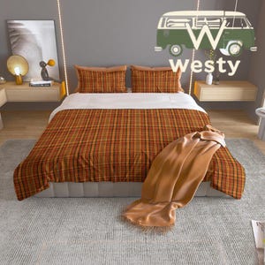 May include: A bed with a plaid orange, brown, and black patterned comforter and pillowcases. A tan blanket with fringe is draped over the bed. The word "westy" is written on the wall with a green van graphic.