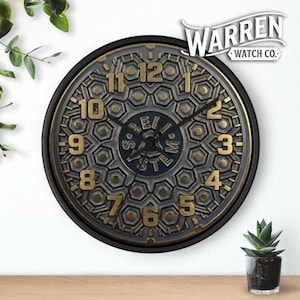May include: A round wall clock with a black frame and a detailed face. The clock face features a gold and gray design with large gold numerals. The clock has the text "Warren Watch Co." at the top.