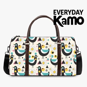 May include: A duffel bag with a cream background featuring a repeating pattern of black, teal, and yellow birds, white daisies, and geometric shapes. The bag has dark brown handles, a black shoulder strap, and the text EVERYDAY Kamo in the corner.