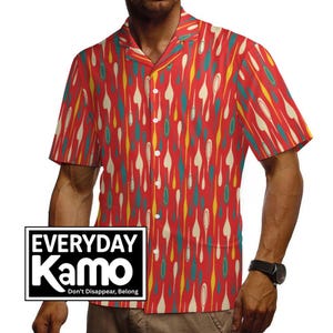 May include: A short-sleeve button-down shirt in a vibrant red color featuring a repeating pattern of elongated teardrop shapes in cream, yellow, and teal. The shirt includes a collar and a white logo box with the text EVERYDAY Kamo Don't Disappear, Belong.
