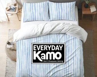 May include: A bed with a white headboard and two matching nightstands. The bedding features a blue and white striped pattern with a white duvet cover. The duvet cover has a black and white rectangular graphic that says "EVERYDAY Kamo" and "Don't Disappear, Belong."