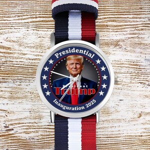 Puede incluir: Un reloj plateado con una banda a rayas azul, blanca y roja. La esfera del reloj presenta un retrato de Donald Trump con el texto "Presidential Trump Inauguration 2025" rodeado de estrellas.