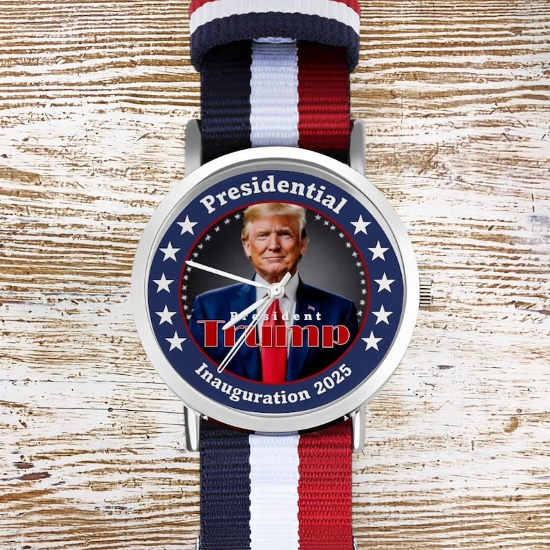Puede incluir: Un reloj plateado con una banda a rayas azul, blanca y roja. La esfera del reloj presenta un retrato de Donald Trump con el texto "Presidential Trump Inauguration 2025" rodeado de estrellas.