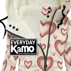 May include: Cream-colored jacket with a heart pattern in shades of pink. The jacket features a hood with a soft, white lining and black drawstrings. The text "EVERYDAY Kamo" is displayed on a white rectangle.