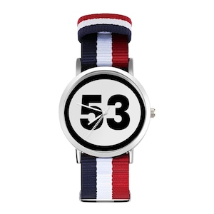 May include: A silver wristwatch with a white face and black numbers. The watch has a red, white, and blue striped nylon band. The face of the watch has the number 53 on it.