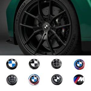 May include: A black alloy wheel with a BMW logo centre cap, set against a green car. The image also shows a selection of BMW centre caps with various designs, including blue, white, and red accents.
