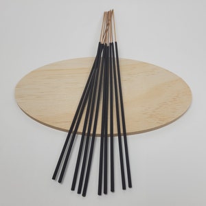 May include: A bundle of black incense sticks with a light brown tip, arranged in a fan shape on a wooden surface.