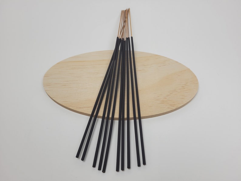 May include: A bundle of black incense sticks with a light brown tip, arranged in a fan shape on a wooden surface.