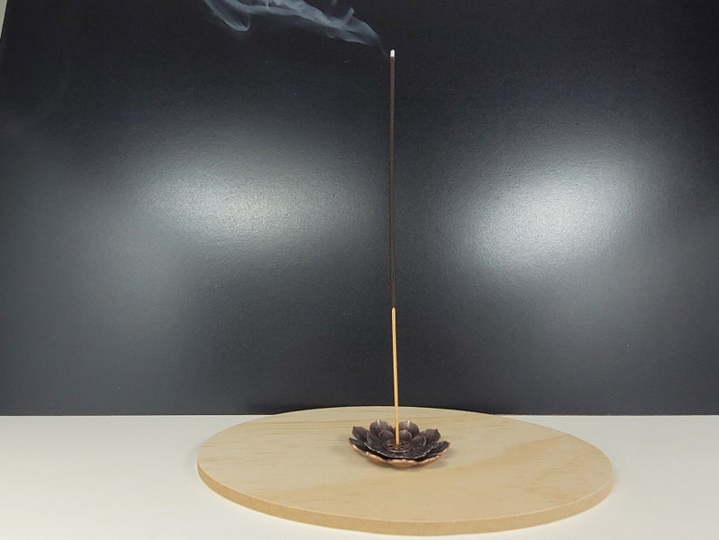 May include: A black incense stick burning in a bronze lotus-shaped incense holder on a wooden base.