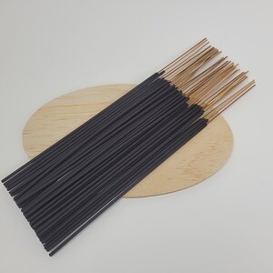 May include: A bundle of black incense sticks with brown tips, arranged on a wooden oval-shaped surface.