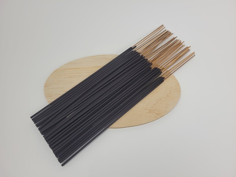 May include: A bundle of black incense sticks with brown tips, arranged on a wooden oval-shaped surface.