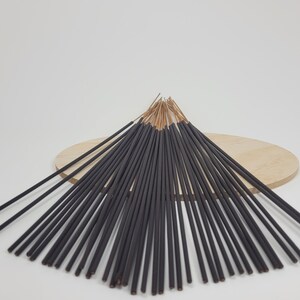 May include: A bundle of black incense sticks with a wooden base. The sticks are arranged in a fan shape and have a natural brown colour at the top.