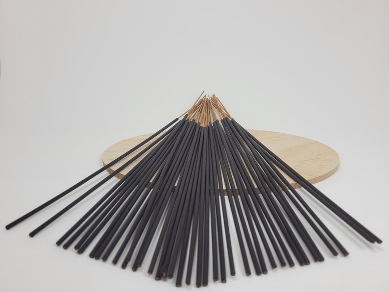 May include: A bundle of black incense sticks with a wooden base. The sticks are arranged in a fan shape and have a natural brown colour at the top.