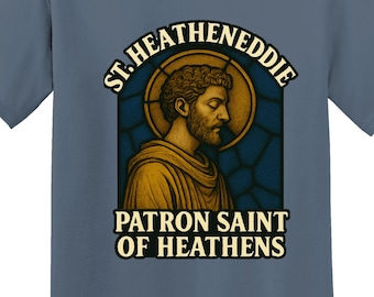 May include: A blue t-shirt featuring a graphic of a saint with the text "ST. HEATENEDDIE PATRON SAINT OF HEATHENS." The saint is depicted in a stained-glass style with a gold halo. The shirt has a crew neck and short sleeves.