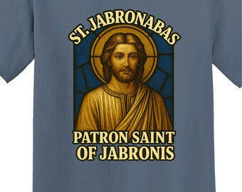 May include: Blue t-shirt featuring a religious-themed graphic. The graphic includes an illustration of a man with a halo, set against a stained-glass window design. Text reads "ST. JABRONABAS PATRON SAINT OF JABRONIS".