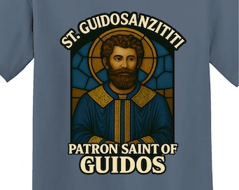 May include: Blue t-shirt featuring a graphic of a saint with a beard, within a stained-glass window design. Text above reads "ST. GUIDOSANZITITI", and below, "PATRON SAINT OF GUIDOS". The shirt has a crew neck and short sleeves.