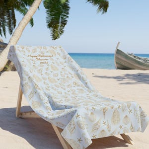 May include: A light blue beach towel with a seashell and starfish pattern. The towel is personalized with the text "Happy Retirement Shannon 2025".