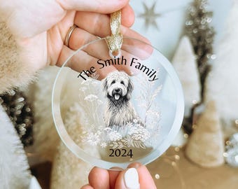 Könnte beinhalten: Ein runder, durchsichtiger Glasanhänger mit einer schwarz-weißen Illustration eines zotteligen Hundes, umgeben von floralen Linienzeichnungen. Der Text "The Smith Family" steht in Schwarz darüber, das Jahr "2024" steht in Schwarz darunter.