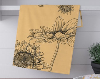Op de afbeelding: Een beige keukendoek met een zwarte zonnebloemillustratie. De doek heeft een groot zonnebloemontwerp met gedetailleerde bloemblaadjes en stelen. Het ontwerp wordt herhaald over de doek.