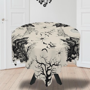May include: A round Halloween-themed tablecloth with a cream background and a black spooky design. The design includes bats, spiders, spiderwebs, a haunted house, and bare trees. The tablecloth is draped over a black table.