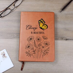 Puede incluir: Un diario marr&oacute;n con la frase "Change is Beautiful" y una mariposa amarilla. Debajo del texto hay un dise&ntilde;o floral. El diario tiene una cinta de marcador marr&oacute;n.