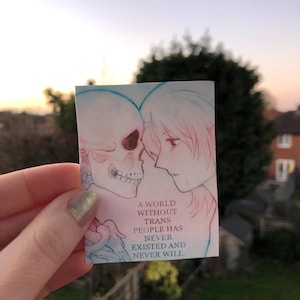 May include: A small rectangular card with a blue and red illustration of a skull and a person's profile, facing each other. The card has the text: "A world without trans people has never existed and never will."