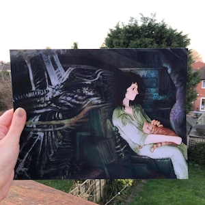 May include: An art print depicting a woman in a green outfit cradling a ginger cat. The artwork has a dark, detailed background with a science fiction theme. The woman is seated, and the cat is in her arms.