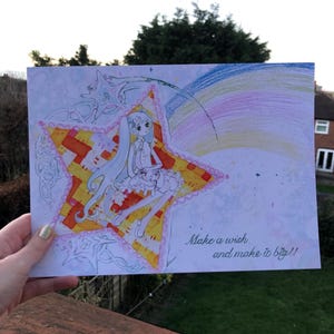 May include: A hand-drawn illustration featuring a cartoon character seated on a star. The star is yellow and orange with a pink border. A rainbow arcs across the top. The text reads, "Make a wish and make it big!!"