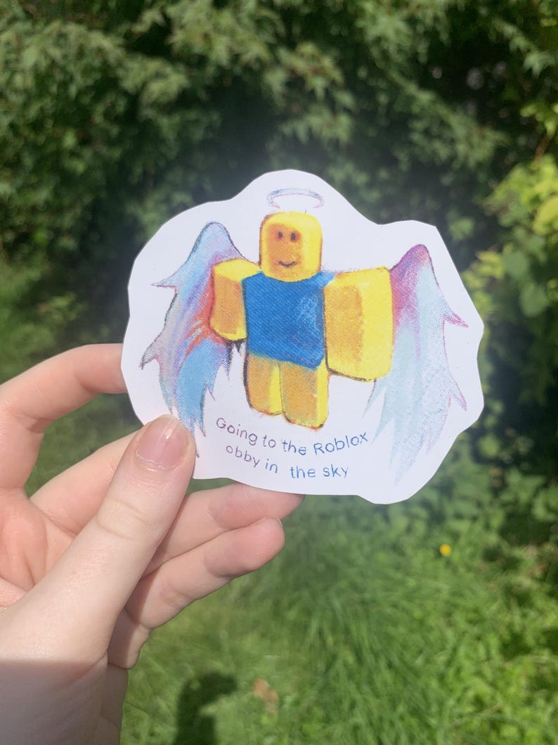 May include: A yellow Roblox character with a blue shirt and halo, wearing angel wings with blue and purple feathers. The sticker reads "Going to the Roblox obby in the sky."