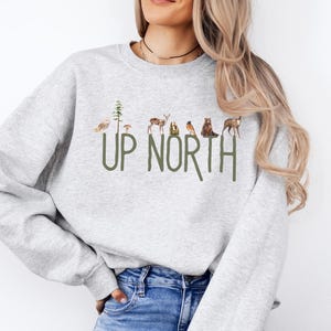 Show your love for the North with our "Up North" sweatshirt. Featuring beautiful watercolor imagery of iconic Midwestern creatures and lush trees, it's perfect for cabin trips, bonfires, or cozy nights at home. Ideal for anyone who cherishes their time in the North, it makes a great gift for nature lovers, outdoor enthusiasts, or those who hold fond memories of their northern adventures at the cabin, lake house, or cottage.