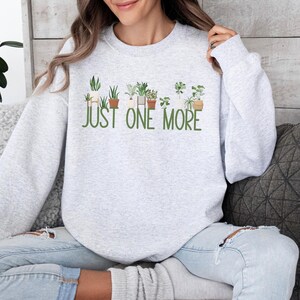May include: A gray sweatshirt with a graphic of potted plants and the text "JUST ONE MORE".