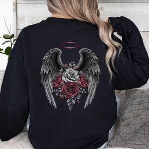 May include: A black long-sleeve sweatshirt featuring a graphic on the back. The design displays a pair of large, detailed gray wings with a red halo above them. Below the wings is a cluster of roses in shades of deep red, pink, and white.