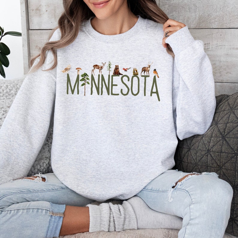 Wrap yourself in Minnesota pride with our "Minnesota Sweatshirt," adorned with picturesque watercolor woodland imagery. Ideal for proud Minnesotans or as a thoughtful gift. Embrace the spirit of the North Star State.