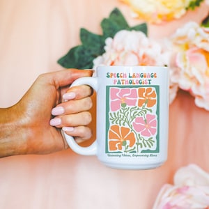 May include: White ceramic mug with a green border and floral design. The text "Speech Language Pathologist" is printed in green and the text "Unlocking Voices, Empowering Lives" is printed in black.