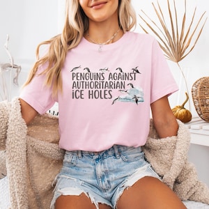 May include: A pink t-shirt with a graphic of penguins and the text "Penguins Against Authoritarian Ice Holes".