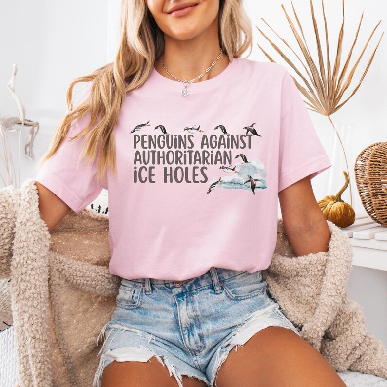 May include: A pink t-shirt with a graphic of penguins and the text "Penguins Against Authoritarian Ice Holes".