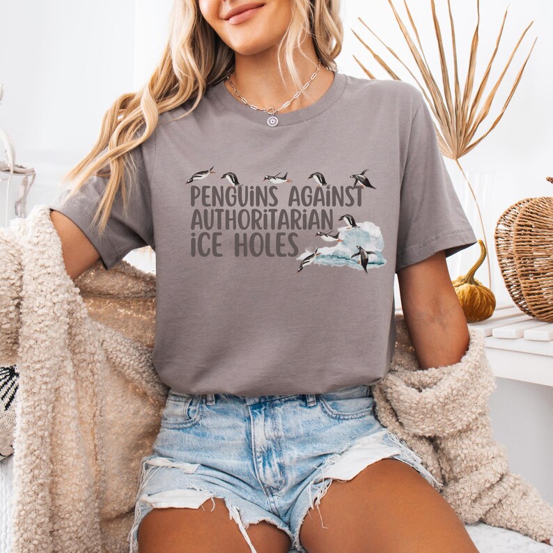 May include: A gray t-shirt with a graphic of penguins jumping over an ice floe. The text "Penguins Against Authoritarian Ice Holes" is printed on the shirt.