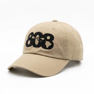 May include: A tan baseball cap featuring the number 808 embroidered in black thread on the front panel. The cap has a structured crown, a curved brim with visible stitching, and a button at the top center. The design is centered on the front.