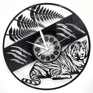 May include: A black and white decorative wall clock featuring a tiger design. The clock is made from a repurposed vinyl record. The clock face has a black and white striped background with a fern design and a tiger illustration.