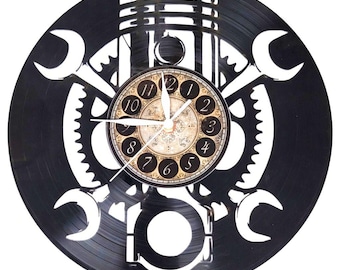 May include: Black wall clock made from a repurposed vinyl record. The clock features a central clock face with a vintage design, surrounded by white cut-out shapes of tools and engine parts. The clock hands are white.