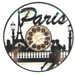 May include: Black circular wall clock with a Paris theme. The clock features a silhouette of the Eiffel Tower, street lamps, and a couple dancing. The clock face has Roman numerals.