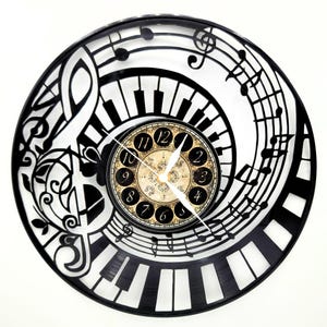 May include: A black and white wall clock with a musical theme. The clock features a piano keyboard design, musical notes, and a vintage-style clock face with Roman numerals. The clock hands are white.