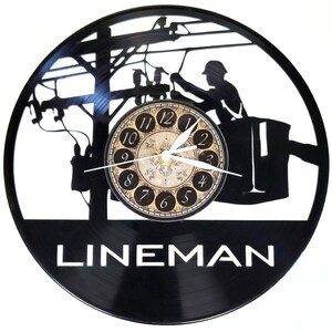 May include: Black vinyl record clock featuring a lineman silhouette working on power lines. The clock face has a decorative design with black numerals and hands. The word "LINEMAN" is displayed in white text at the bottom.