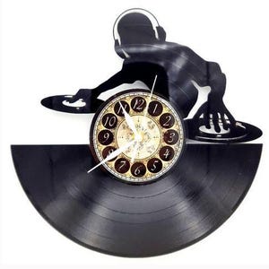 May include: A black vinyl record clock featuring a silhouette of a DJ with headphones. The clock face has a vintage design with Roman numerals and hands pointing to the time. The clock is a unique decorative item.