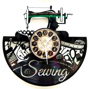 May include: A black and white wall clock with a sewing theme. The clock face is round with Roman numerals. The clock's design includes a sewing machine, scissors, buttons, and the word "Sewing".