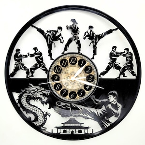 May include: Black and white wall clock featuring martial arts figures in action poses. The clock face is a classic design with Roman numerals. A dragon and pagoda are also depicted in the design. The clock is a unique decorative item.
